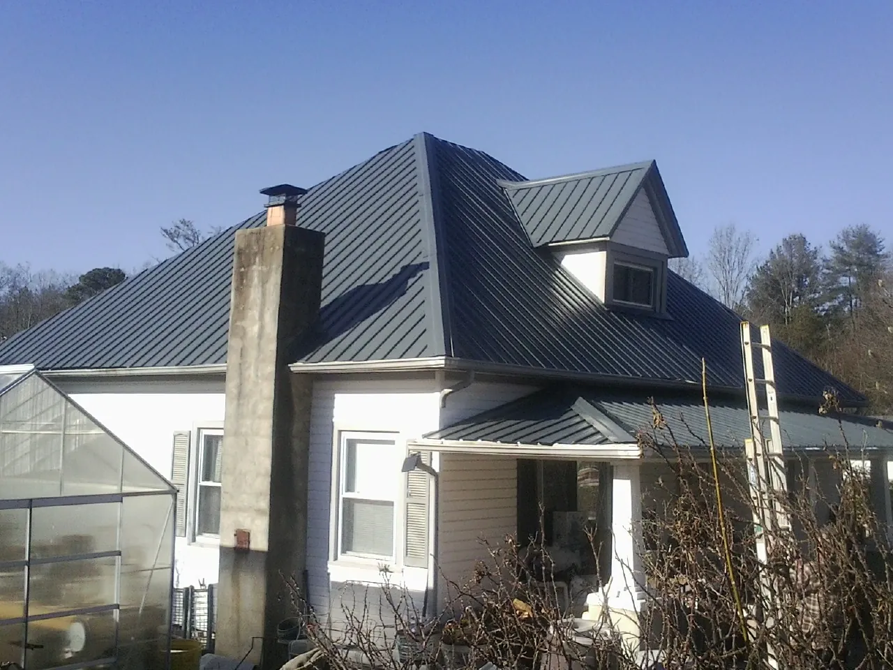 Dark blue standing seam metal roof on a white farmhouse with dormer — Slate & Tile Roof Repair by Roofing Brothers in Ruthville