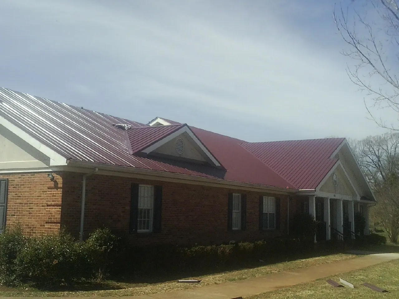 Red metal roof with gabled entries on a long brick building, from a Hail Damage Roof Repair job in Ruthville