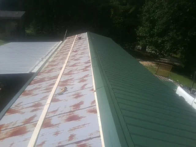 Old rusted panels beside newly installed green metal roofing — Wind Damage Roof Repair by Roofing Brothers in Ruthville