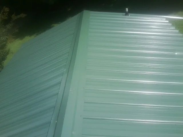 New green metal panels meeting at the ridge of a roof — Flat Roof Repair work by our crew in Ruthville