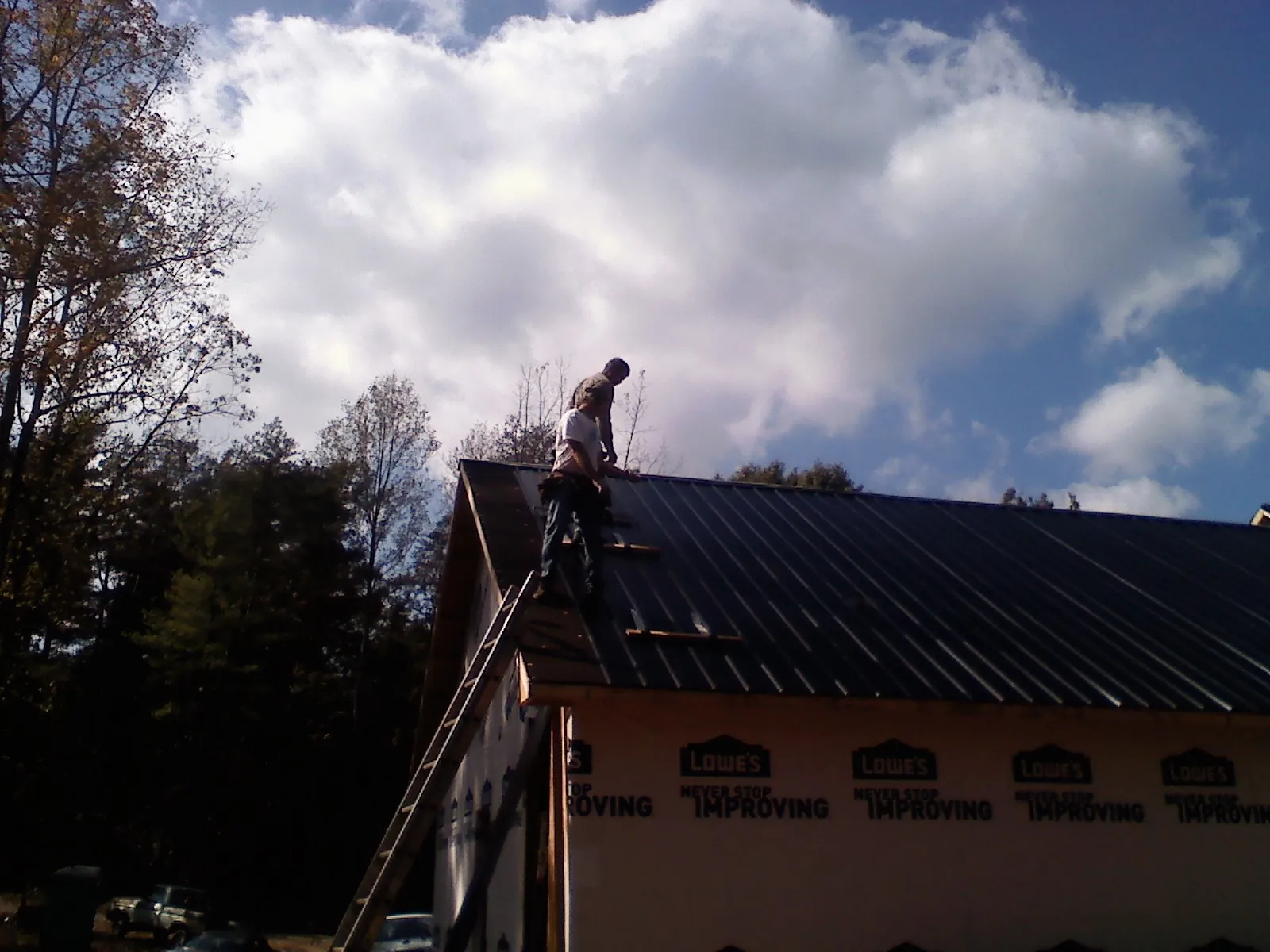 Roofer fastening dark metal panels high against a cloudy sky, from a Roof Inspection job in Ruthville
