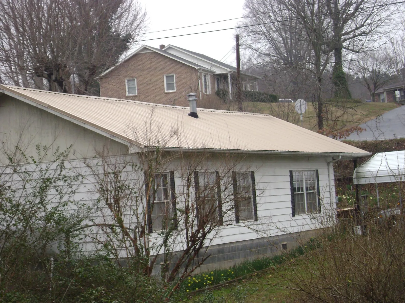 Tan metal roof on a white sided house set into a hillside — Commercial Roofing by Roofing Brothers in Ruthville