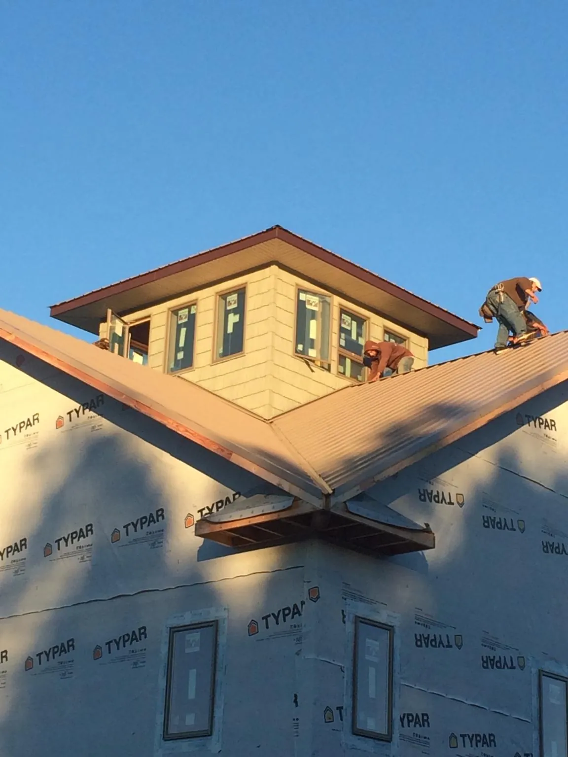 Roofers working around a rooftop cupola on a new metal roof at sunset in Ruthville